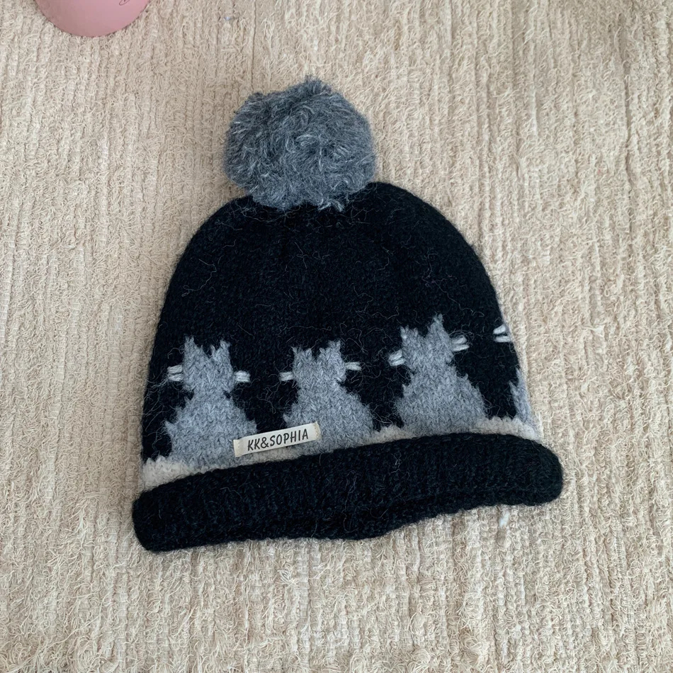 Black and gray knit cat beanie with pom-pom on a beige surface