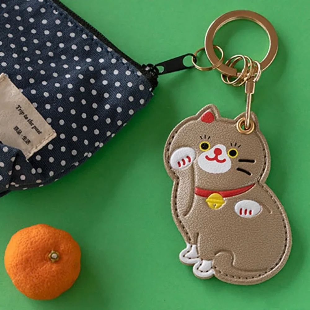 Cat-shaped keychain with a polka dot pouch and orange on a green background