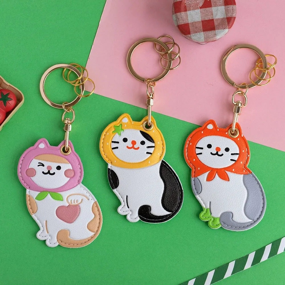 Three cat-themed keychains on a green and pink background