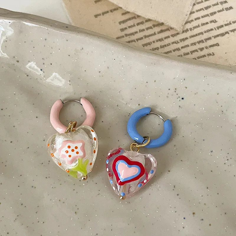 Heart-shaped earrings with colorful designs on a speckled surface.