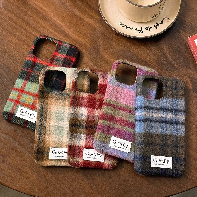 Four plaid phone cases with camera cutouts are arranged on a wooden table. Each case has a different colorway of plaid pattern and a small white label near the bottom with the brand name 'GURVIER'.
