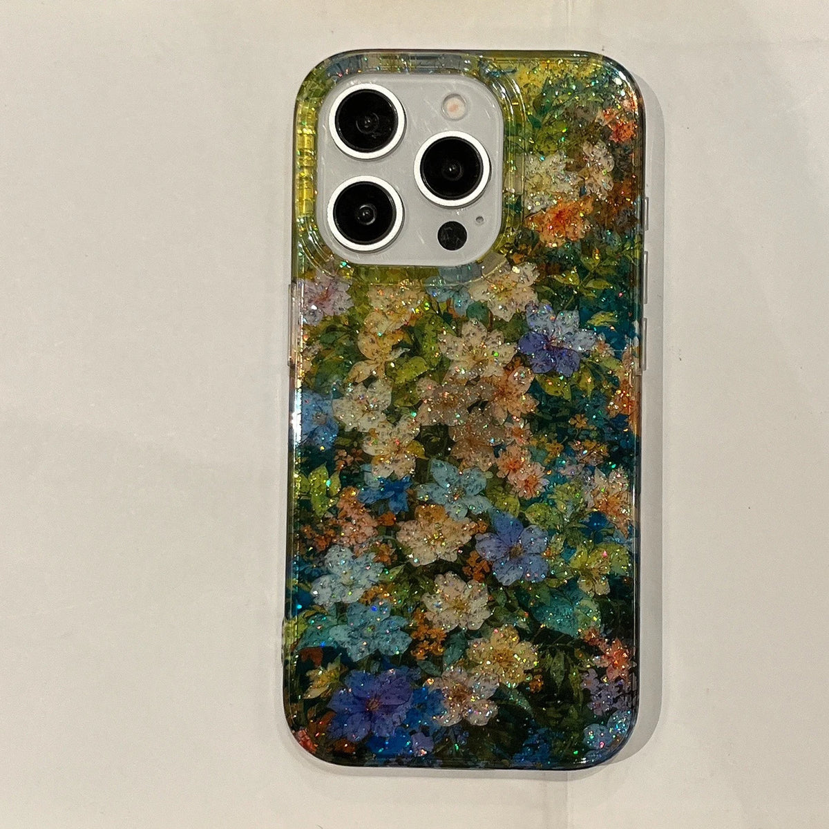 A clear phone case with a dense, colorful floral pattern and embedded glitter, shown on a light-colored phone against a neutral background.