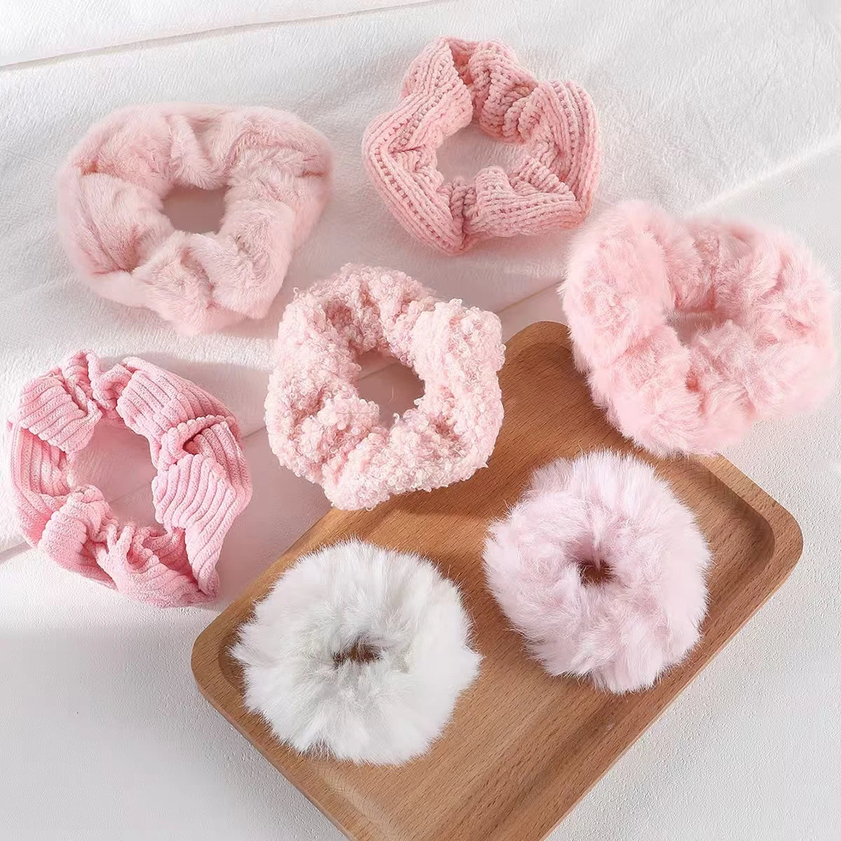Set of pink and white textured scrunchies on a wooden tray.