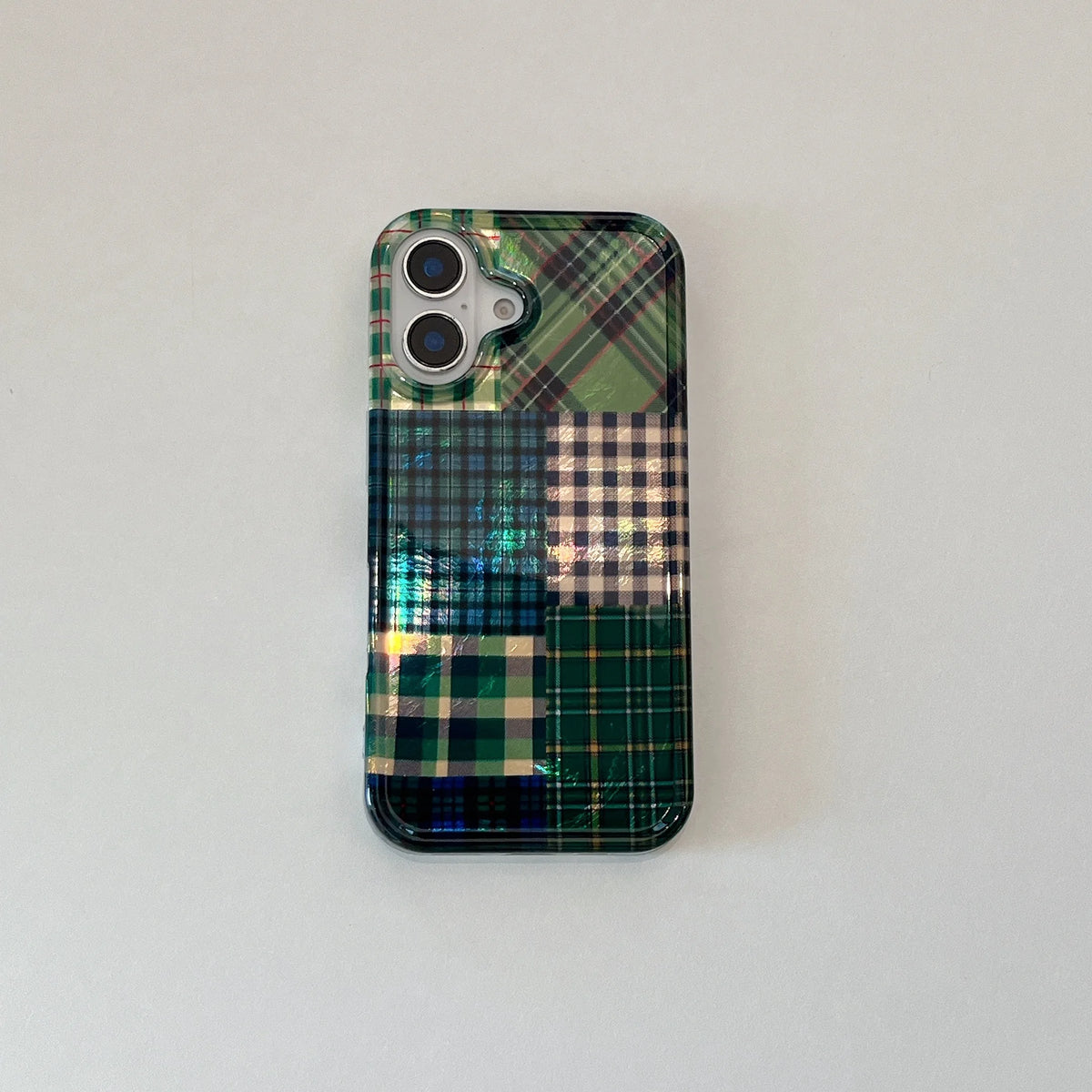 A phone case featuring a patchwork design of green, blue, and beige tartan plaid patterns, shown on a light gray background.