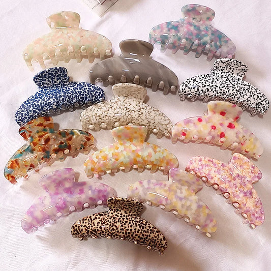 A set of ten hair claw clips arranged on a white fabric background, featuring various patterns including leopard print, marble, and solid colors.