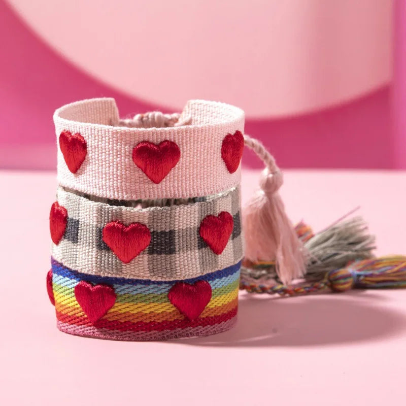 Colorful woven bracelet with red heart patterns on a pink background