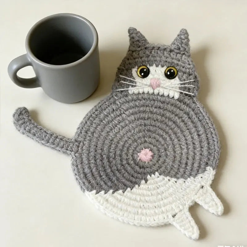 Cat-shaped crochet coaster next to a gray mug on a light background