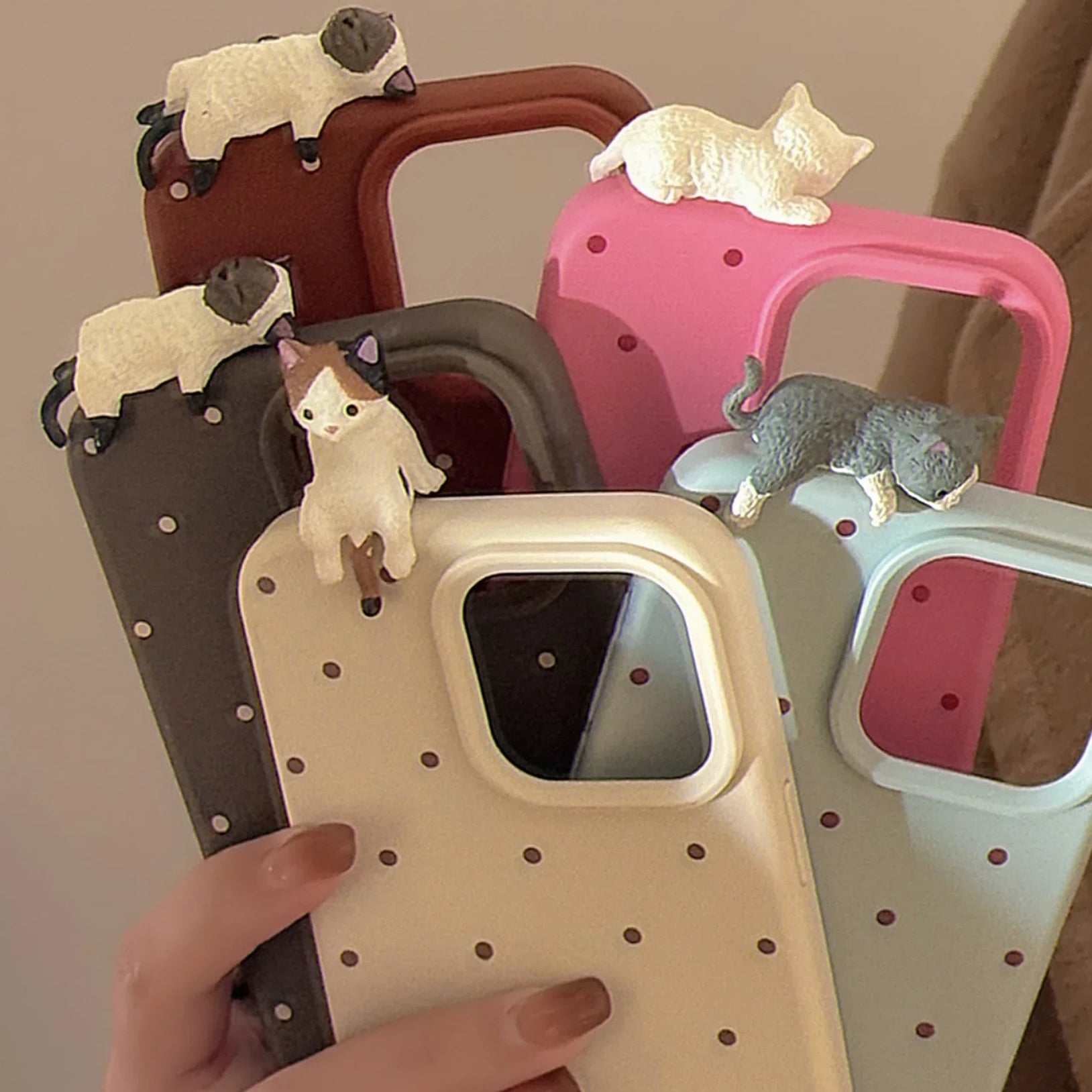 Set of phone cases with cat figurines on handles, held by a hand.