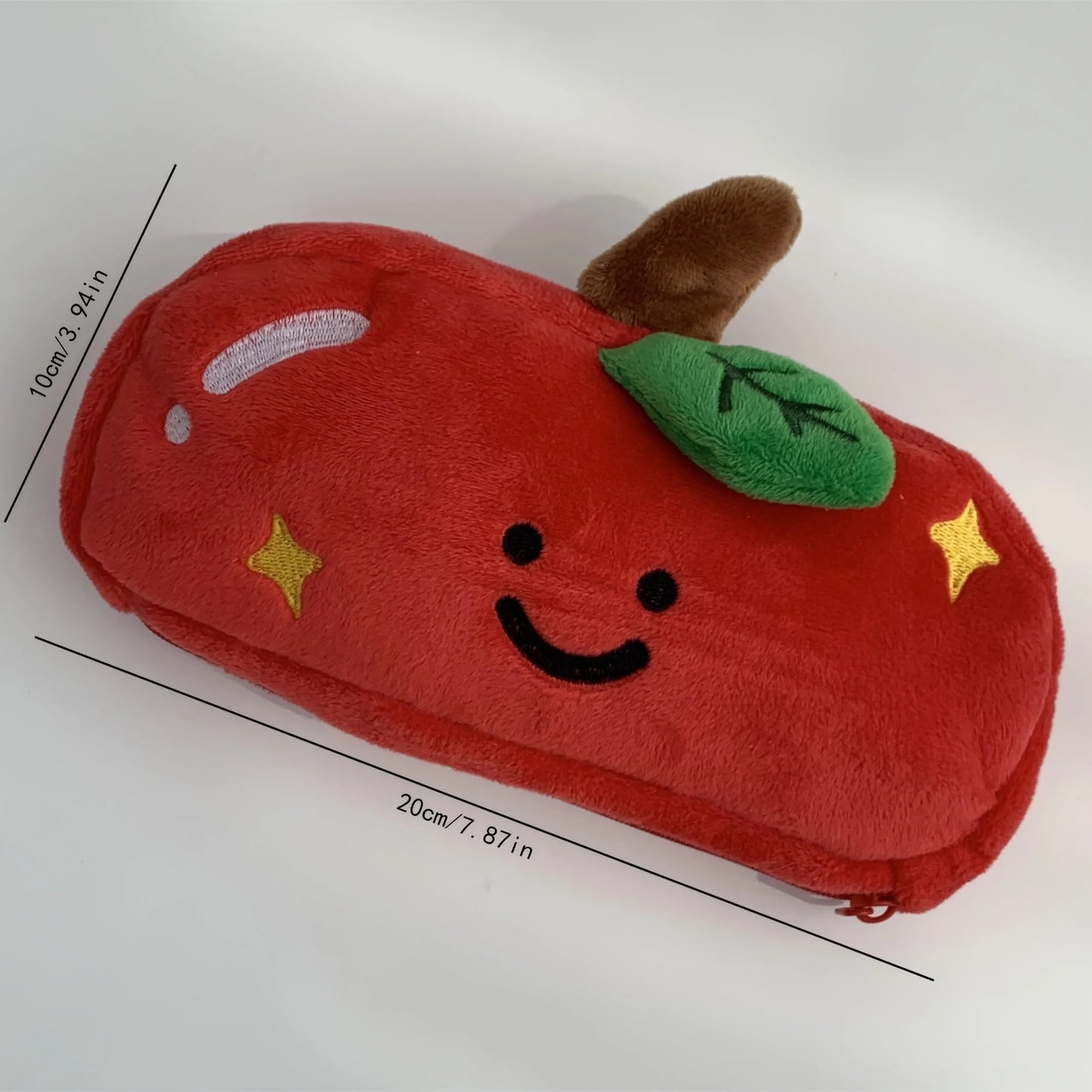 A red plush apple-shaped pencil case with embroidered facial features, a green leaf, a brown stem, and yellow star accents, shown on a white background with black dimension lines and text indicating measurements.