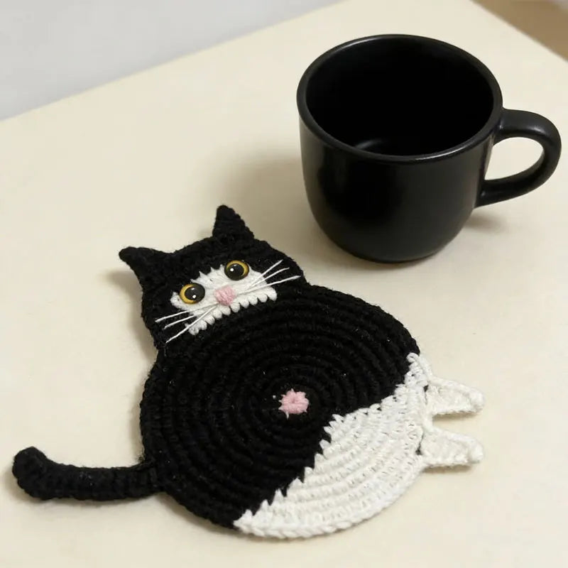 Cat-shaped crocheted trivet next to a black mug on a light surface