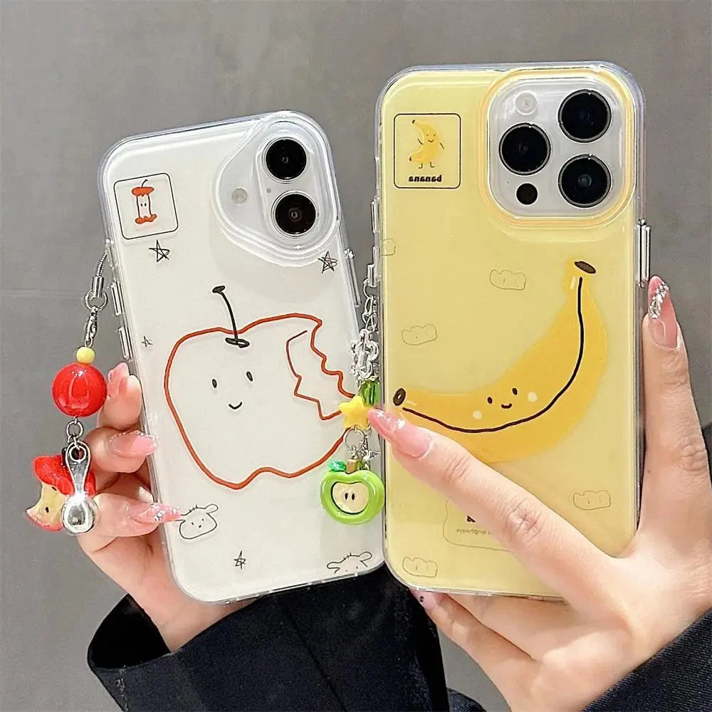 Two transparent phone cases held in hands against a gray background. The left case is clear with a red apple outline and small decorative doodles, including a red and green dangling charm.