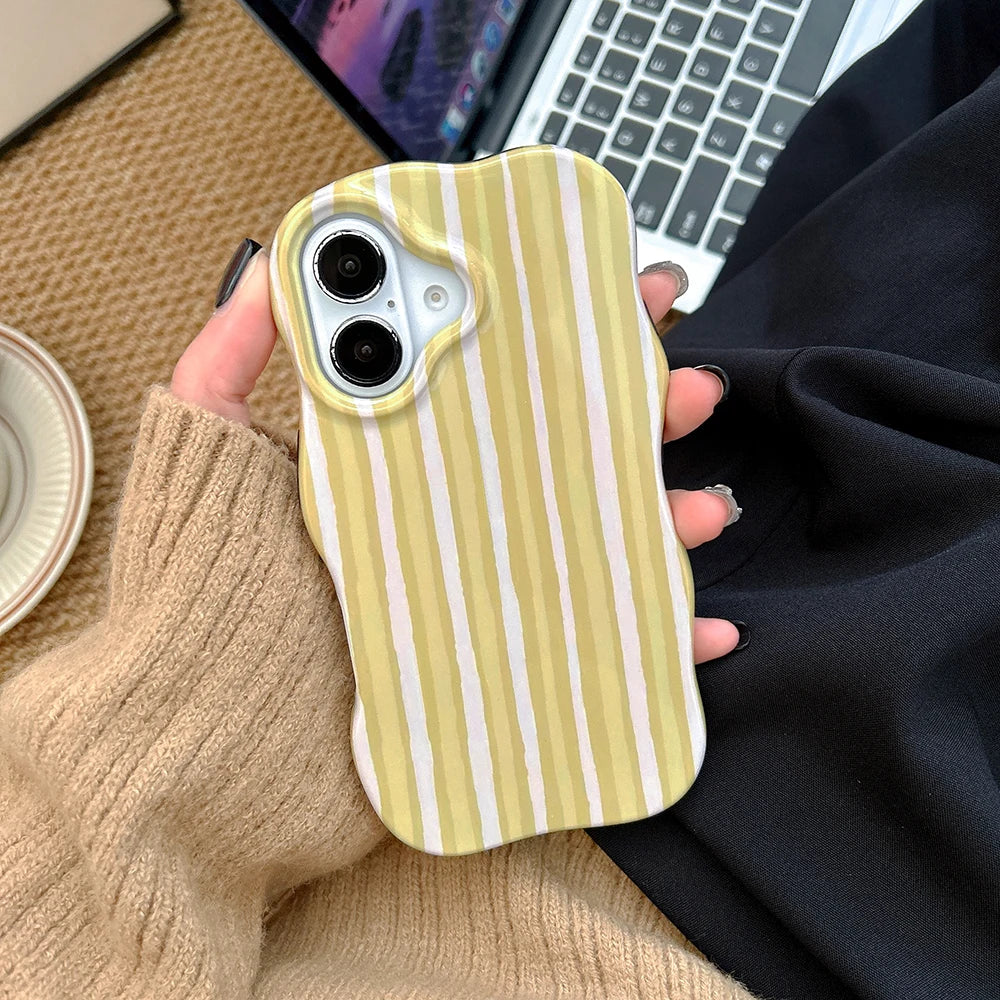 Hand holding a phone with a yellow and white striped case, blurred laptop in the background