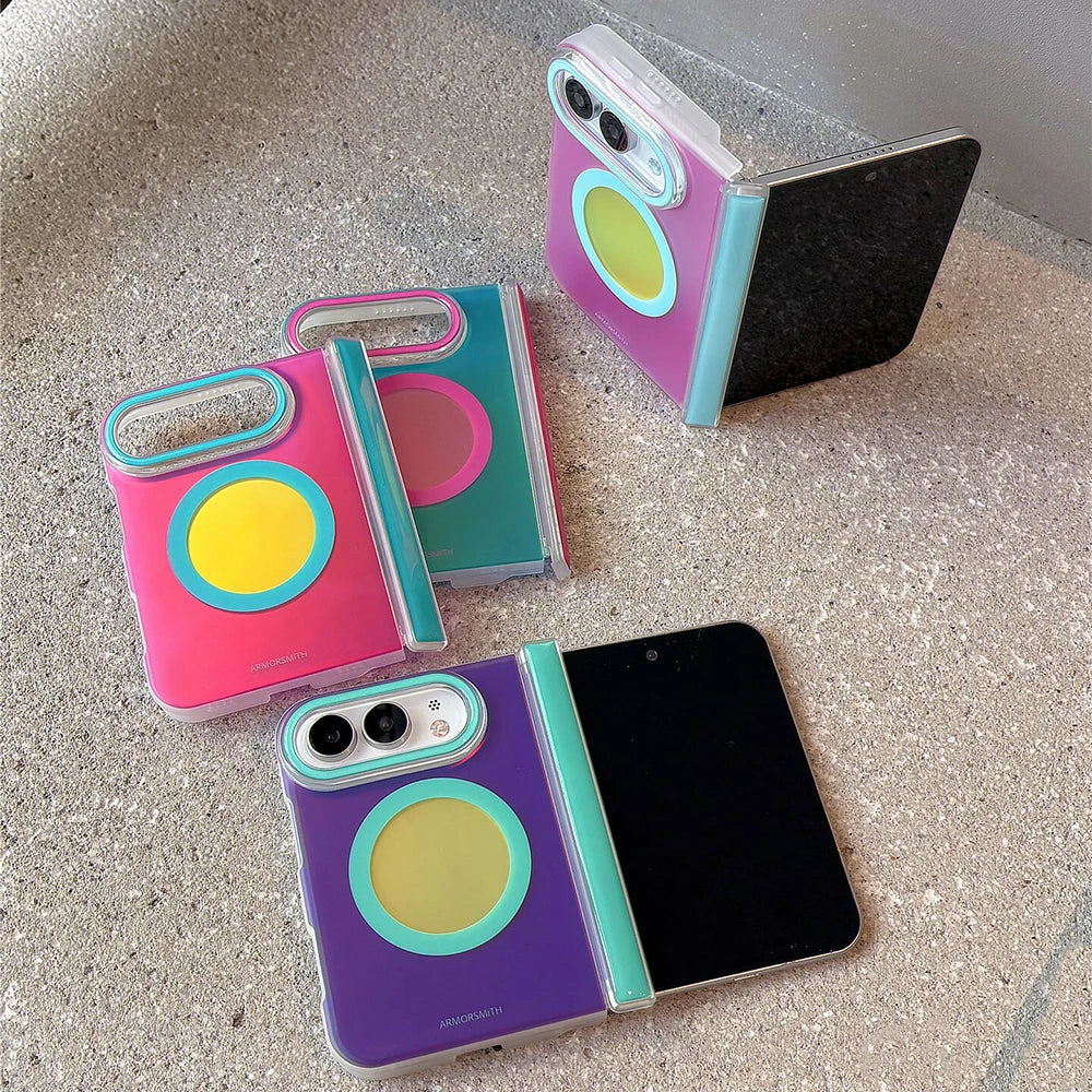 Three colorful foldable phone cases shown open and closed on a textured stone surface. The cases feature a translucent clear back with a large circular magnetic ring in yellow, teal, pink, and purple, plus matching accent rings around the camera cutout and side hinge.