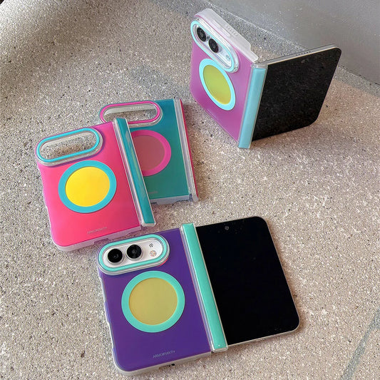 Three colorful foldable phone cases shown open and closed on a textured stone surface. The cases feature a translucent clear back with a large circular magnetic ring in yellow, teal, pink, and purple, plus matching accent rings around the camera cutout and side hinge.