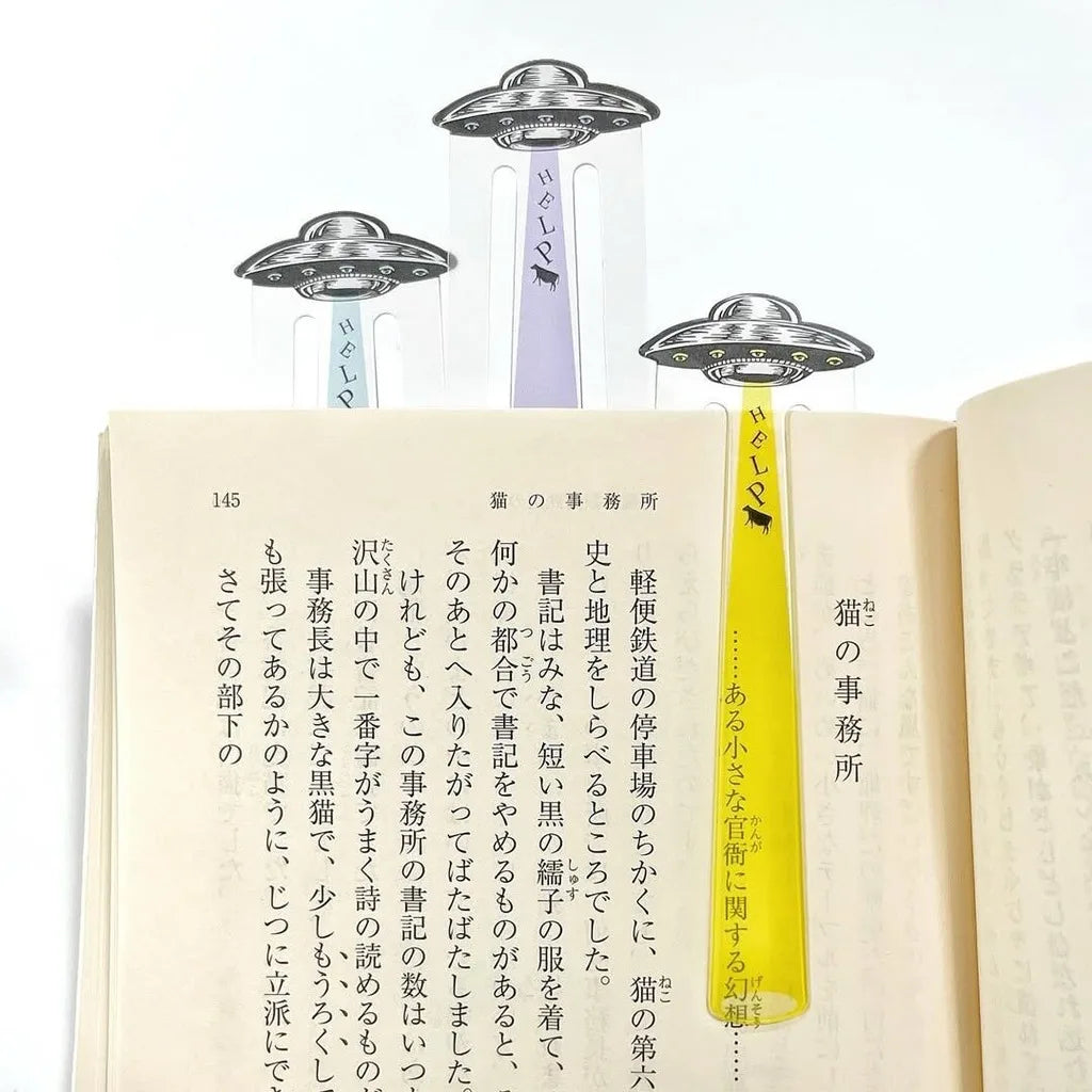 Three UFO-shaped book spacers with Japanese text and small black cow silhouettes, shown inserted into open books on a white background.