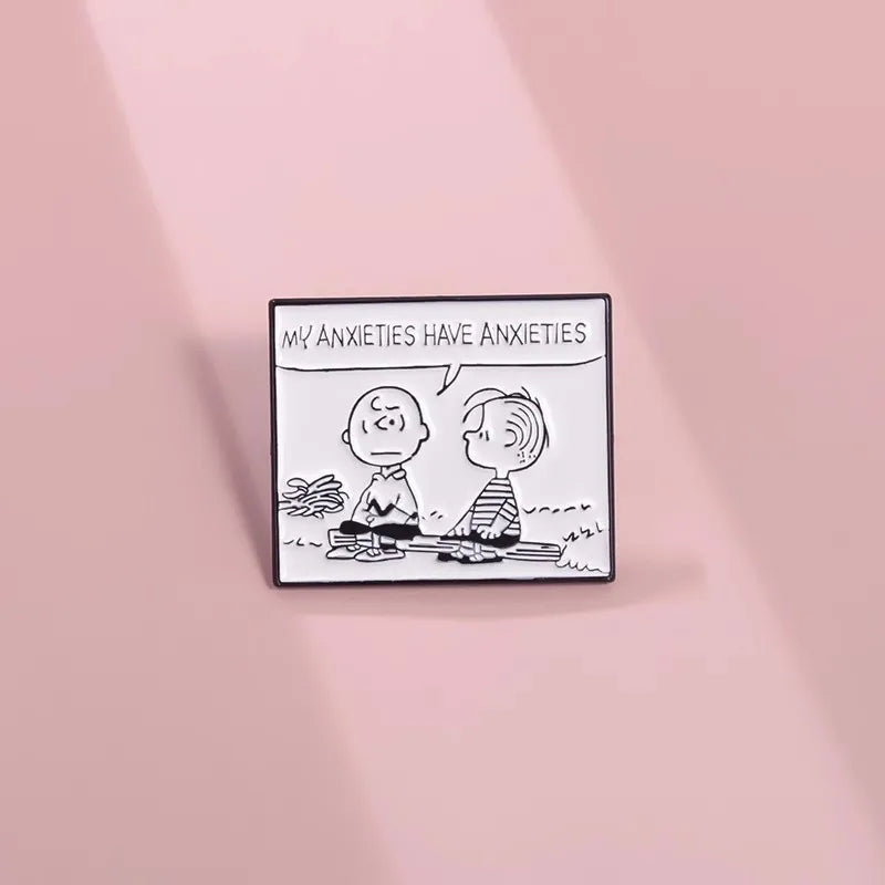 A square enamel pin featuring a black and white cartoon illustration of two characters with the text 'MY ANXIETIES HAVE ANXIETIES' above them, displayed on a soft pink background.