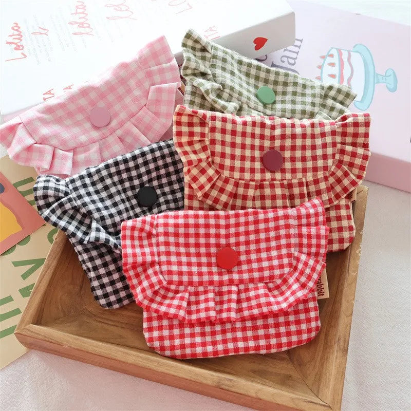 Four gingham ruffled mini purses in pink, green, black-and-white, and red patterns, arranged on a wooden tray with a gift box in the background.