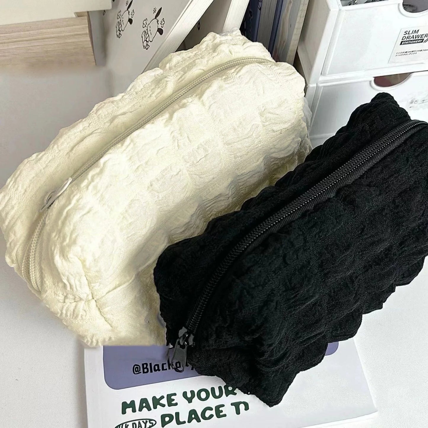 White and black puffy pencil cases on a white surface with a visible brand tag.