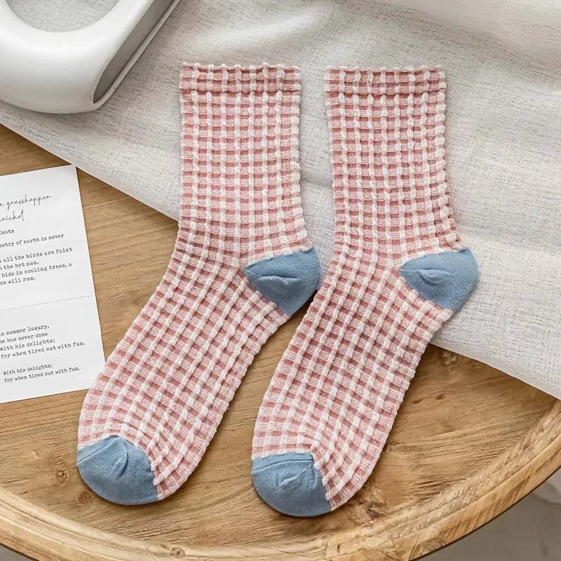 Pair of pink checkered socks with blue toes on a wooden surface.