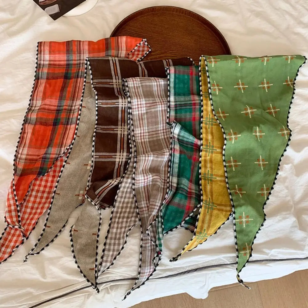 Six colorful plaid and checkered bandanas with black zigzag trim are arranged on a white bed, with a round wooden tray visible in the background.