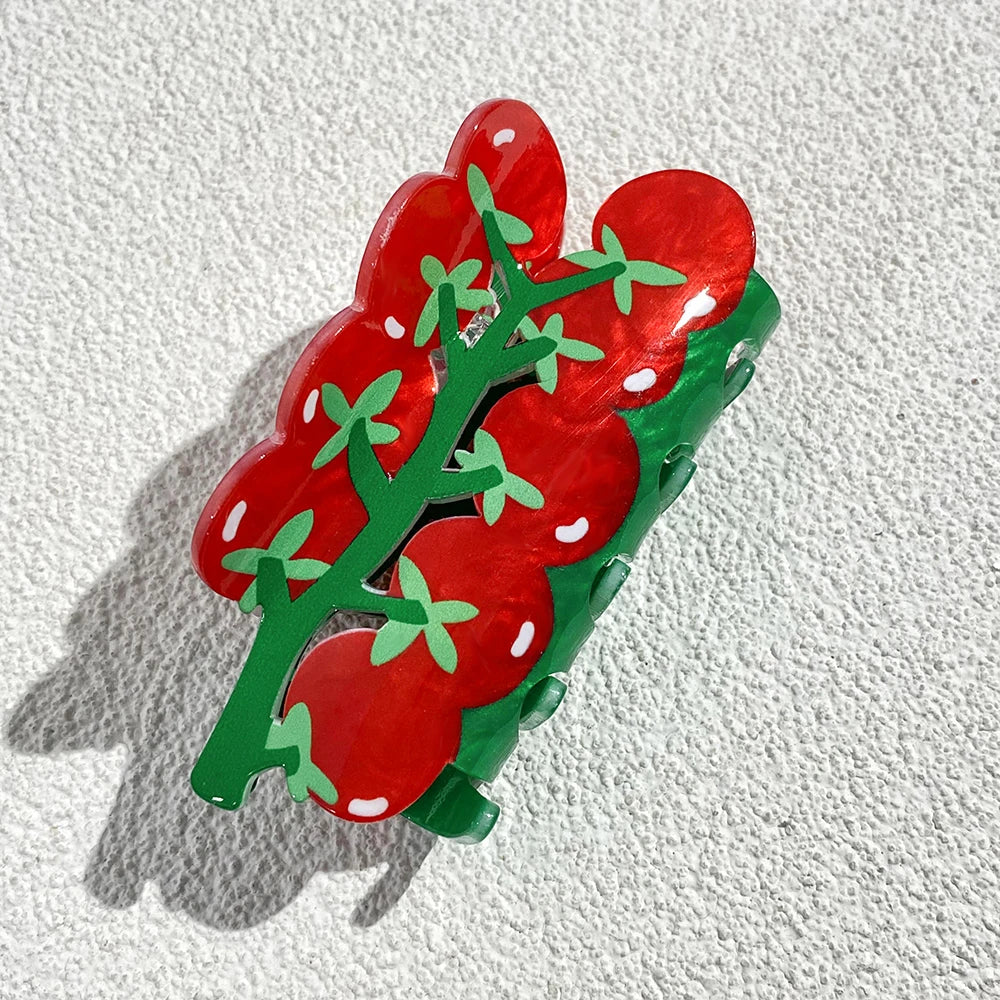 Red tomato-shaped hair clip with green stems on a textured white background