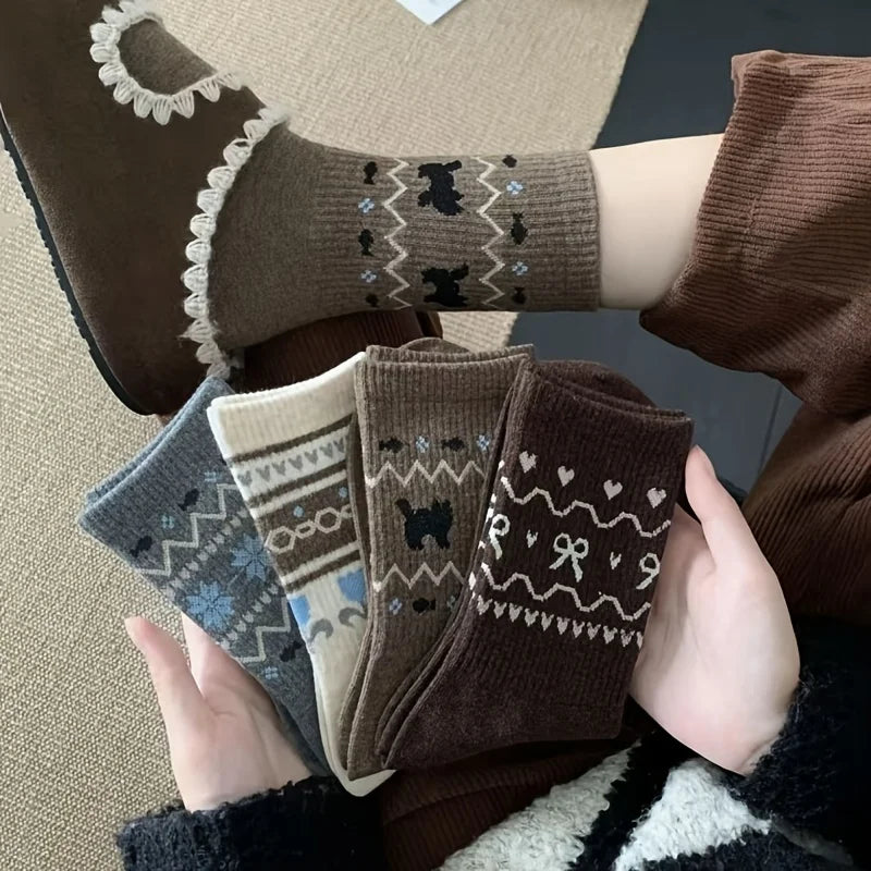 A person holds four pairs of patterned knit socks in brown, cream, gray, and dark brown tones, with one sock also shown worn on a foot. The socks feature winter motifs like snowflakes, hearts, bows, and bears.
