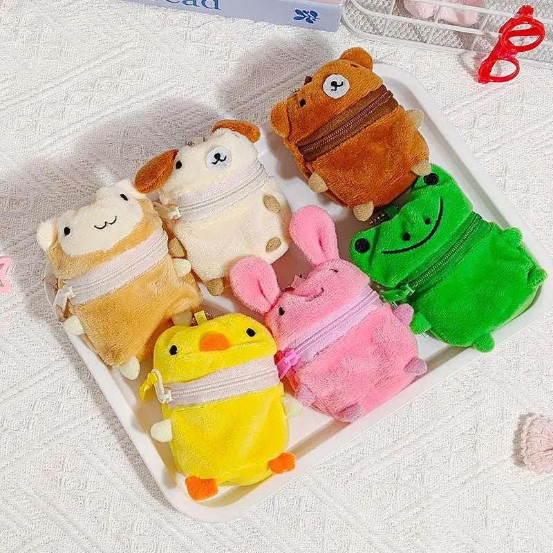 Six small plush character zip pouches arranged on a white tray. The pouches are shaped like a cat, a sheep, a bear, a frog, a duck, and a bunny, in tan, cream, brown, green, yellow, and pink colors.