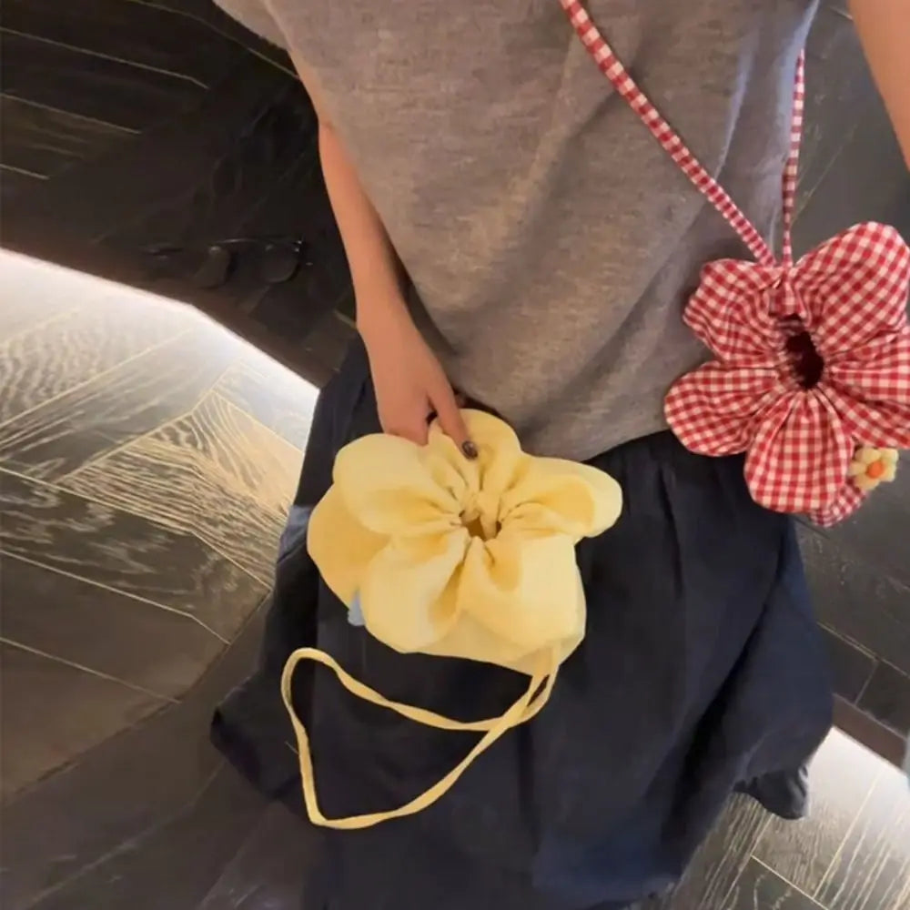 Person holding a yellow flower-shaped bag with another red and white checkered bag in the background.