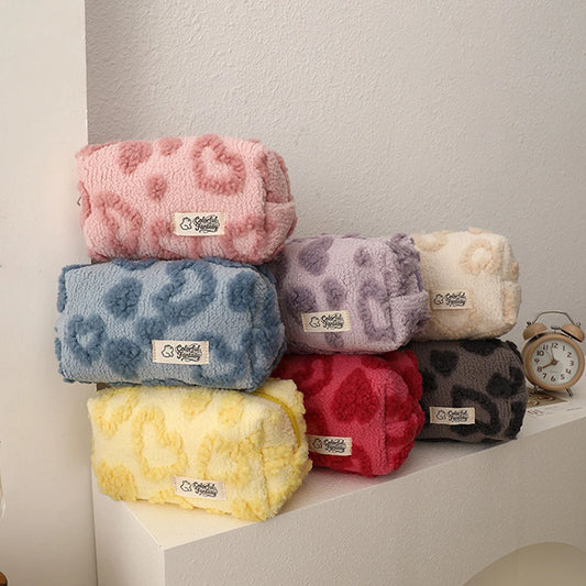 Stack of colorful fleece zipper pouches with brand labels on a shelf.