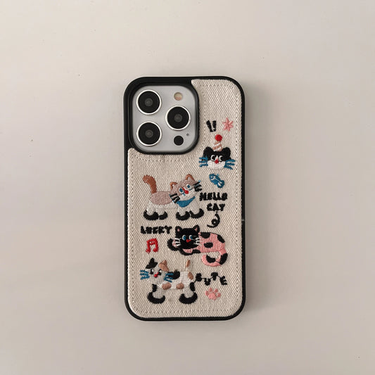 A beige canvas phone case with black trim and colorful embroidered cat illustrations and text, shown on a light gray background.