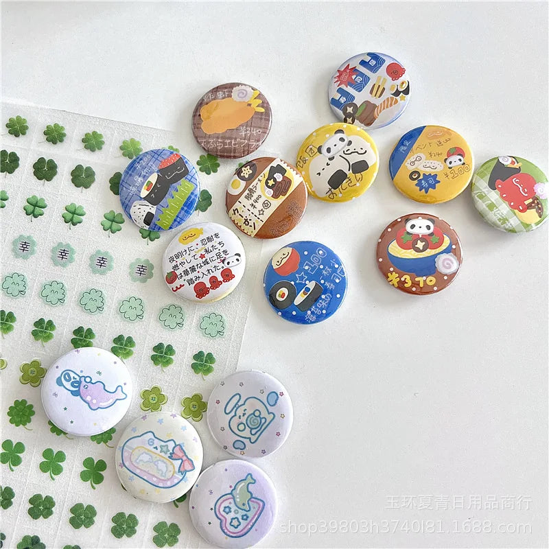 A collection of round pinback buttons with various cartoon and food illustrations, arranged on a white surface alongside a sheet of green four-leaf clover stickers.