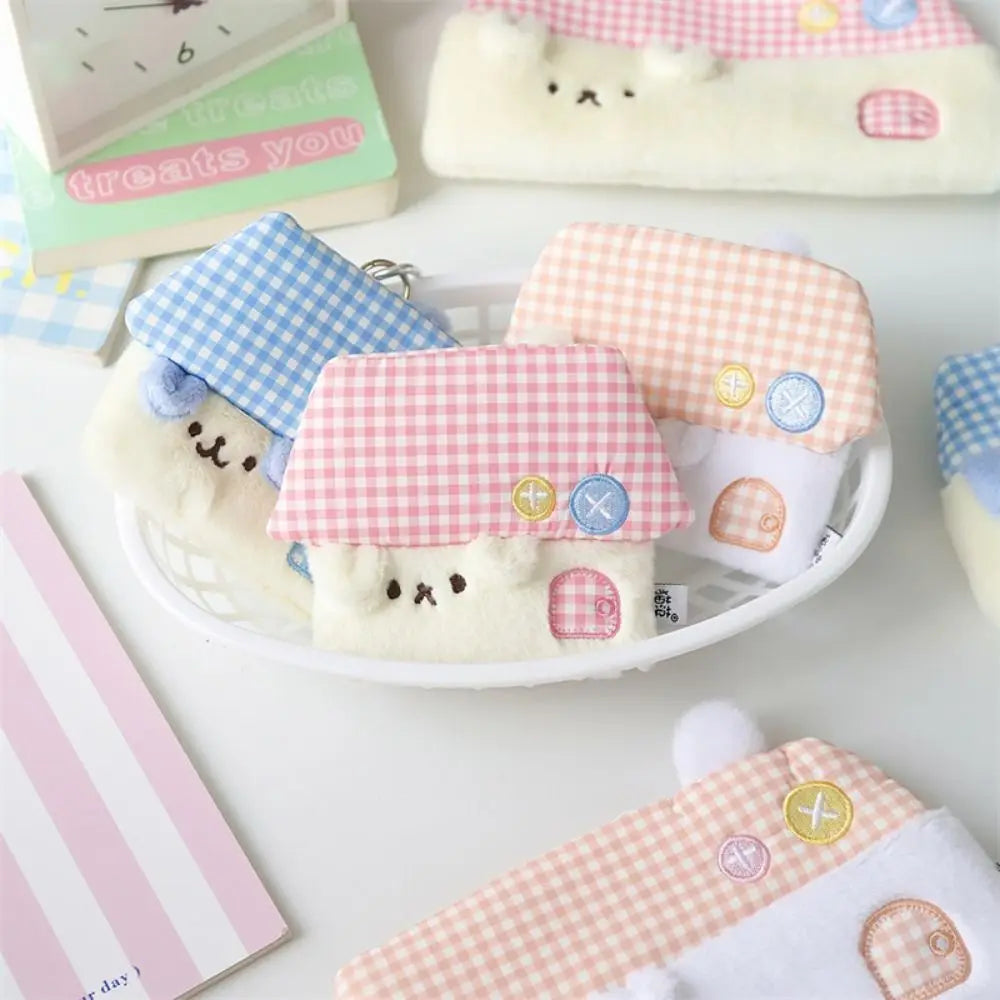 A set of cute, small plush house-shaped coin purses with animal faces, arranged in a white basket on a light surface. The purses feature pink and blue gingham roofs, white plush bodies, embroidered facial features, and small decorative buttons.