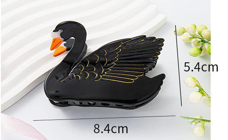 Black swan-shaped hair claw clip with gold wing detailing and an orange beak, shown with dimension labels of 8.4cm length and 5.