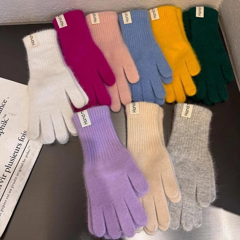 Nine pairs of fuzzy knit gloves in assorted colors, including white, magenta, pink, blue, yellow, green, lavender, cream, and heather gray, arranged on a dark surface. Each pair has a small white fabric label with the brand name 'harori' visible.