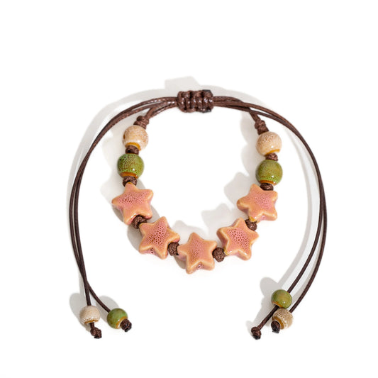 A handmade beaded necklace featuring five pink starfish-shaped beads and green and beige wooden beads on a brown cord, displayed on a clean white background.
