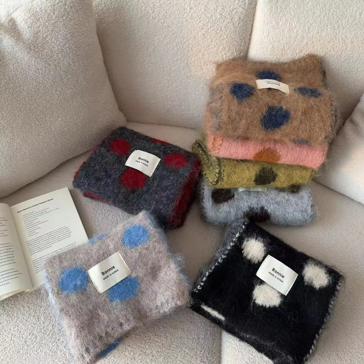 Stack of colorful folded scarves on a beige couch with an open book.