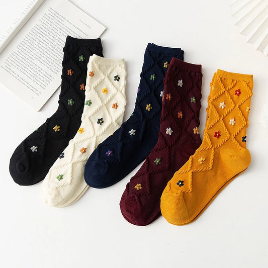 Five pairs of ankle socks arranged in a fan shape on a white background, featuring a textured knit pattern with small embroidered flowers. The colors are black, cream, navy blue, burgundy, and mustard yellow.