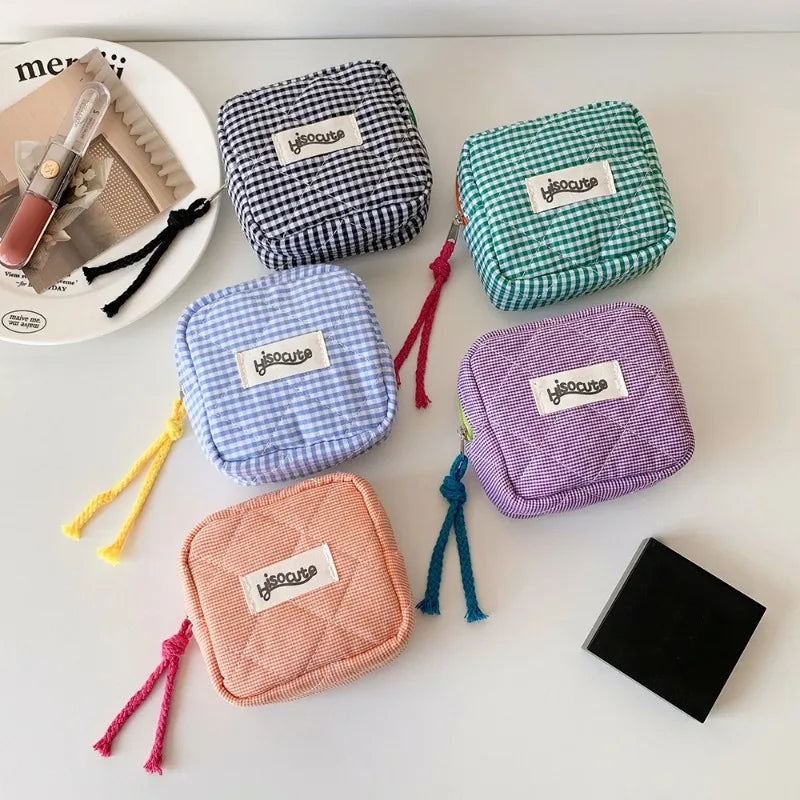 Five small square zip pouches in different checkered and quilted fabric colors are arranged on a white surface. The pouches come in navy-and-white gingham, teal-and-white gingham, light blue-and-white gingham, lavender-and-white gingham, and peach-and-white gingham, each with a small white label reading 'yloooose' and a colorful tassel zipper pull.