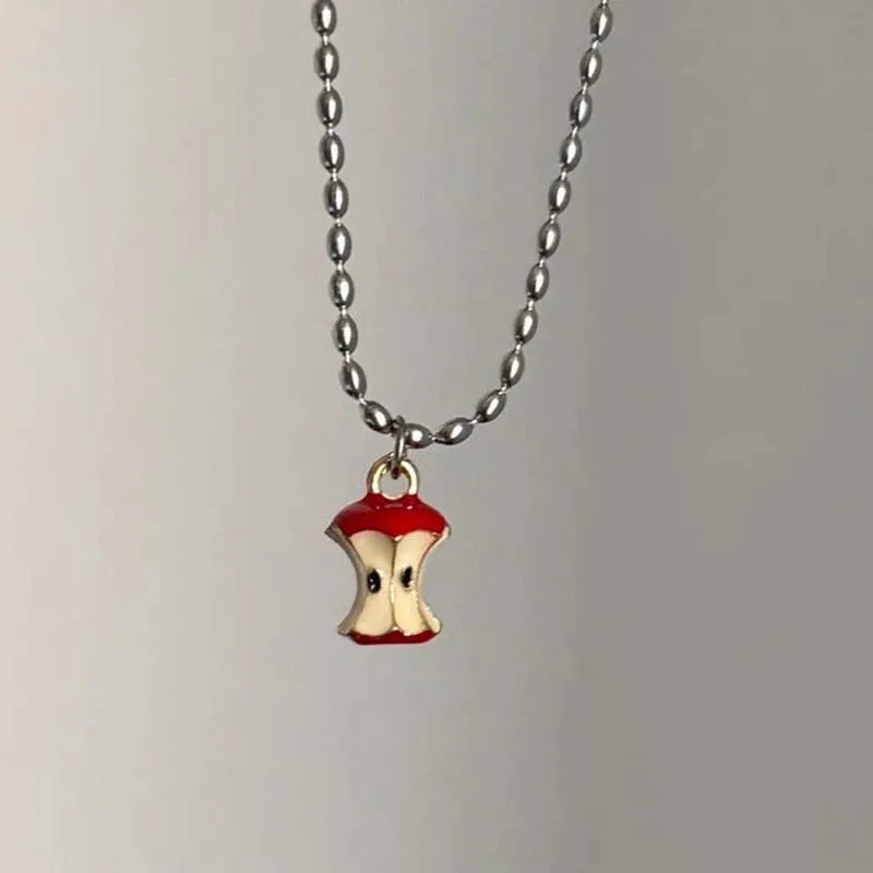 Necklace with a small red and gold apple core pendant on a plain background