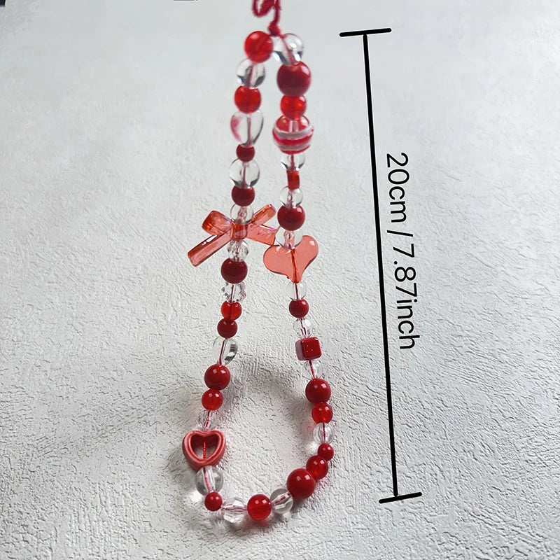 Red and clear acrylic bead phone strap with heart and bow charms, shown on a light textured background with a black measurement line indicating 20cm (7.87 inches) length.