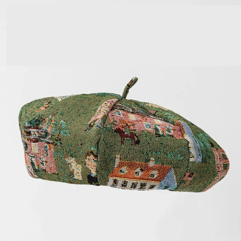 A vintage green woven tapestry hat, likely a 19th-century felt or woven hat, featuring a detailed landscape scene of houses and trees in muted red, orange, blue, and beige tones on a green background.
