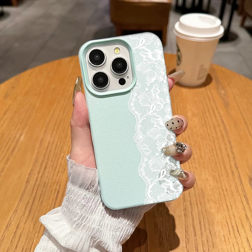 A hand holds a light mint green phone case with a white lace panel on the back, shown over a wooden table with a coffee cup in the background.