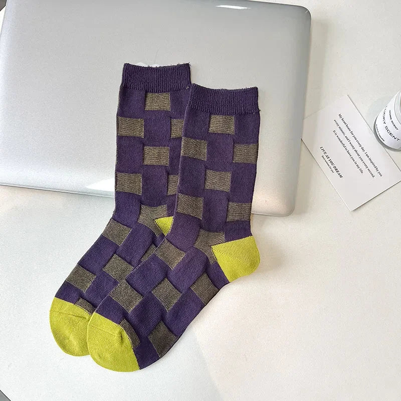 Pair of checkered socks with purple and green pattern on a white surface.