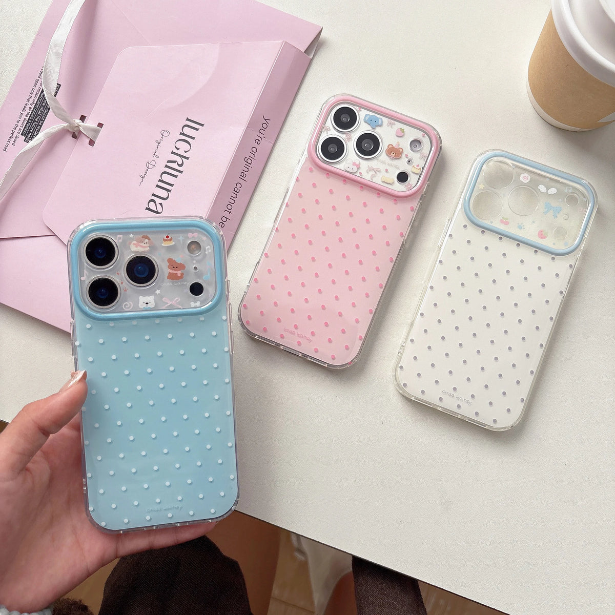 Three polka dot phone cases on a table with a pink box and coffee cup in the background.