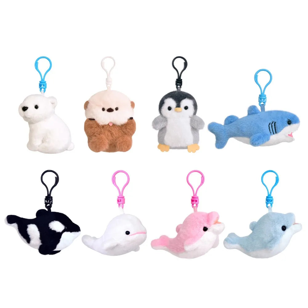 Eight small plush sea-creature and animal keychain charms arranged in two rows on a plain white background. The set includes a white polar bear, a brown teddy bear, a penguin, a blue shark, a black-and-white orca, a white beluga whale, a pink dolphin, and a light blue dolphin, each attached to a plastic clip in blue, black, white, pink, and blue.