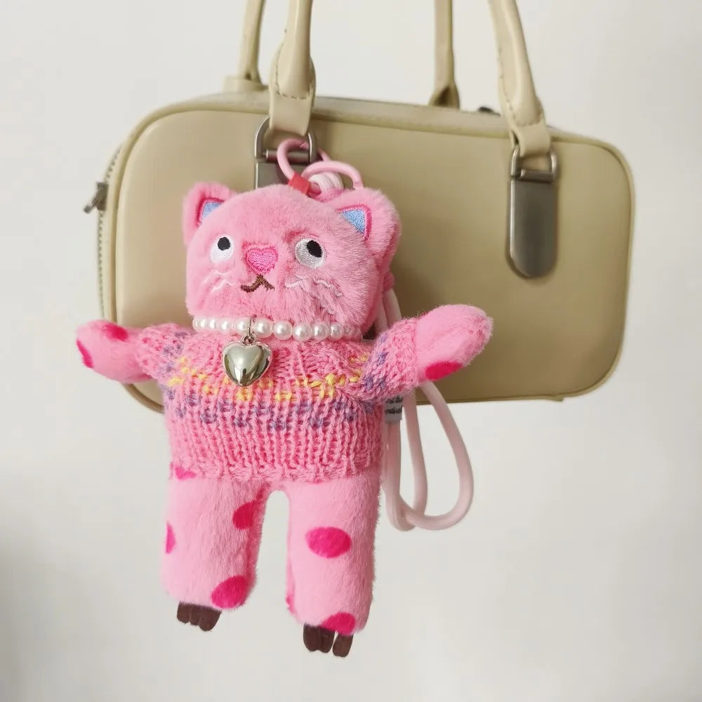 Pink plush toy with a heart pendant attached to a beige handbag.