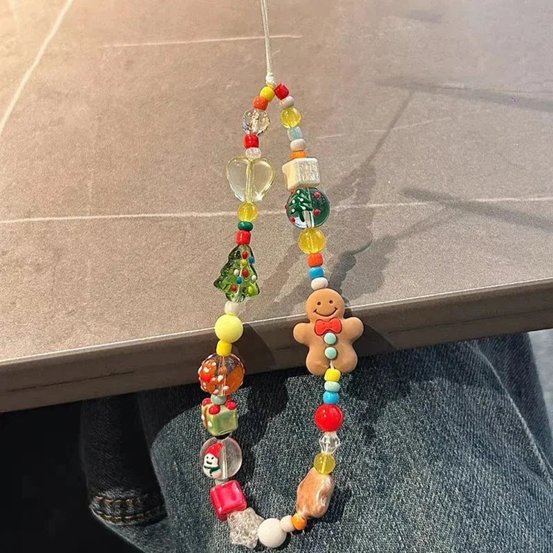 A colorful Christmas-themed beaded phone strap with a gingerbread man charm, resting on a person's lap next to a gray tiled table.