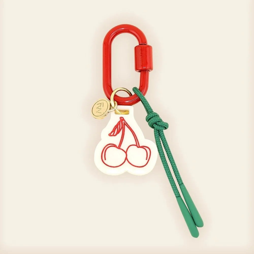Keychain with red carabiner, green strap, and cherry design on a beige background