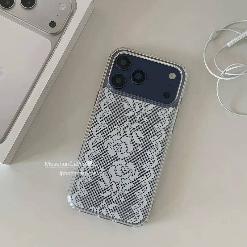 A clear iPhone case with a white floral lace pattern, shown on a phone lying on a light beige surface next to a phone box and earphones.