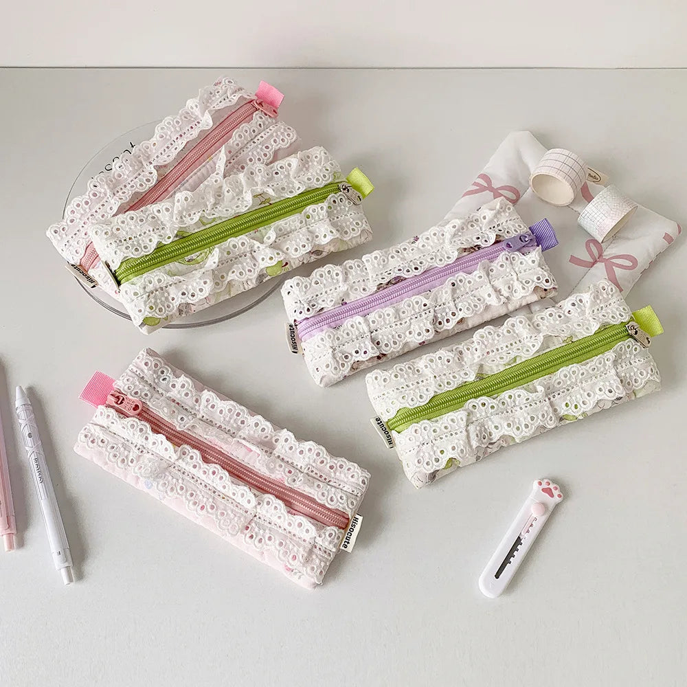Four white lace pencil cases with colorful zippers arranged on a light gray surface, alongside matching stationery props including pens, tape, and a small pouch.